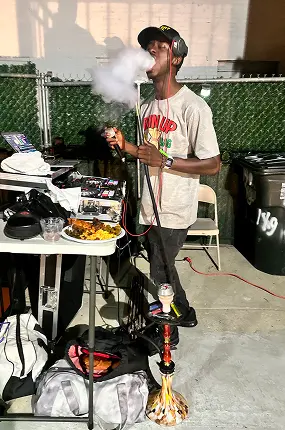 Guest smoking hookah at an outdoor event next to the hookah maker's service station