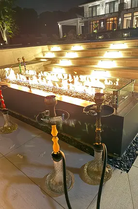 Three hookahs standing by a gas fire pit on a lit terrace at night during a private event